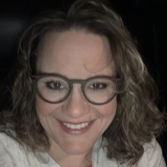 Selfie of a smiling white woman with glasses and curly shoulder-length hair